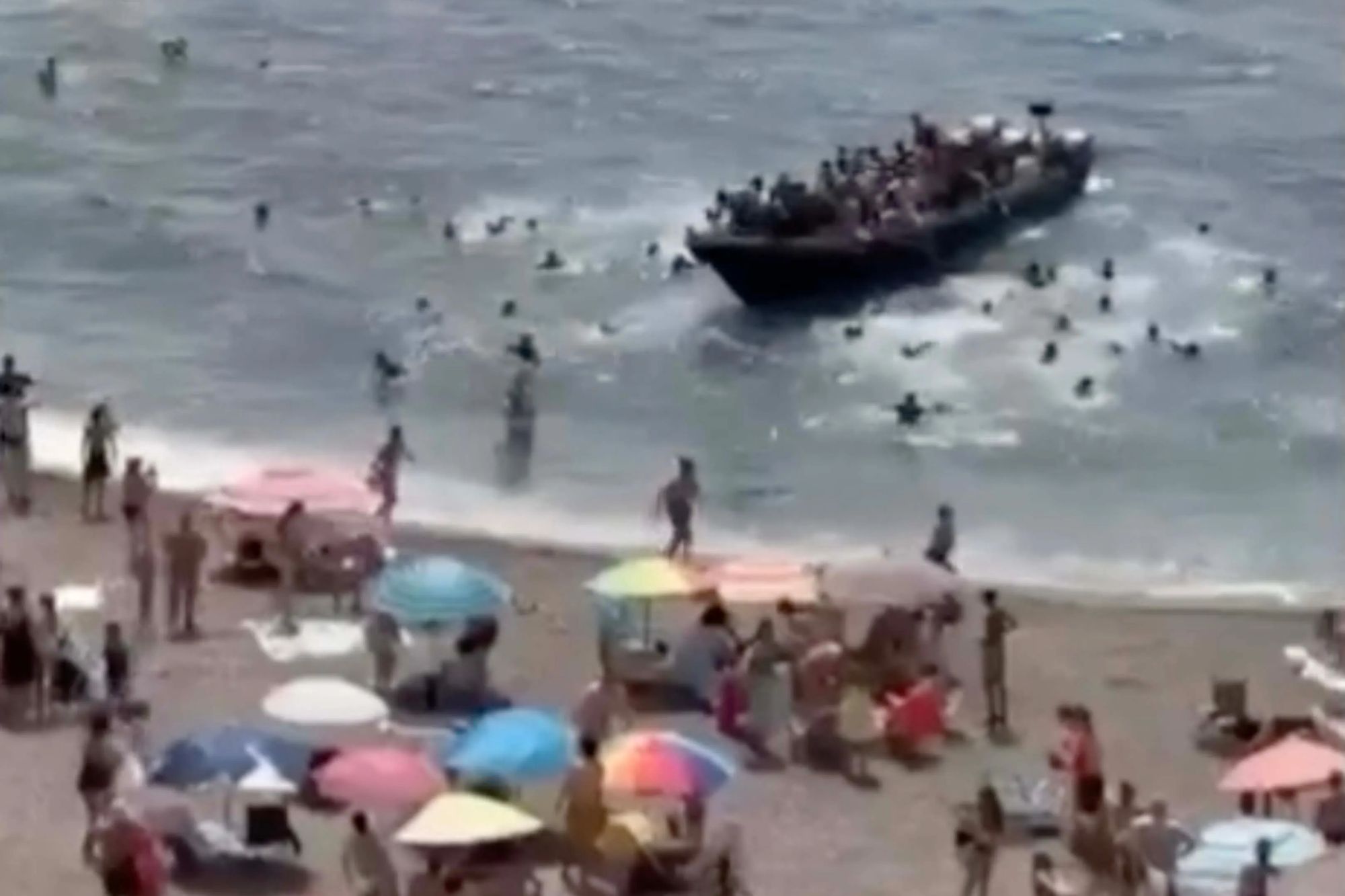 Shocking moment dozens of migrants storm beach packed with tourists in Spain as stunned holidaymakers call cops